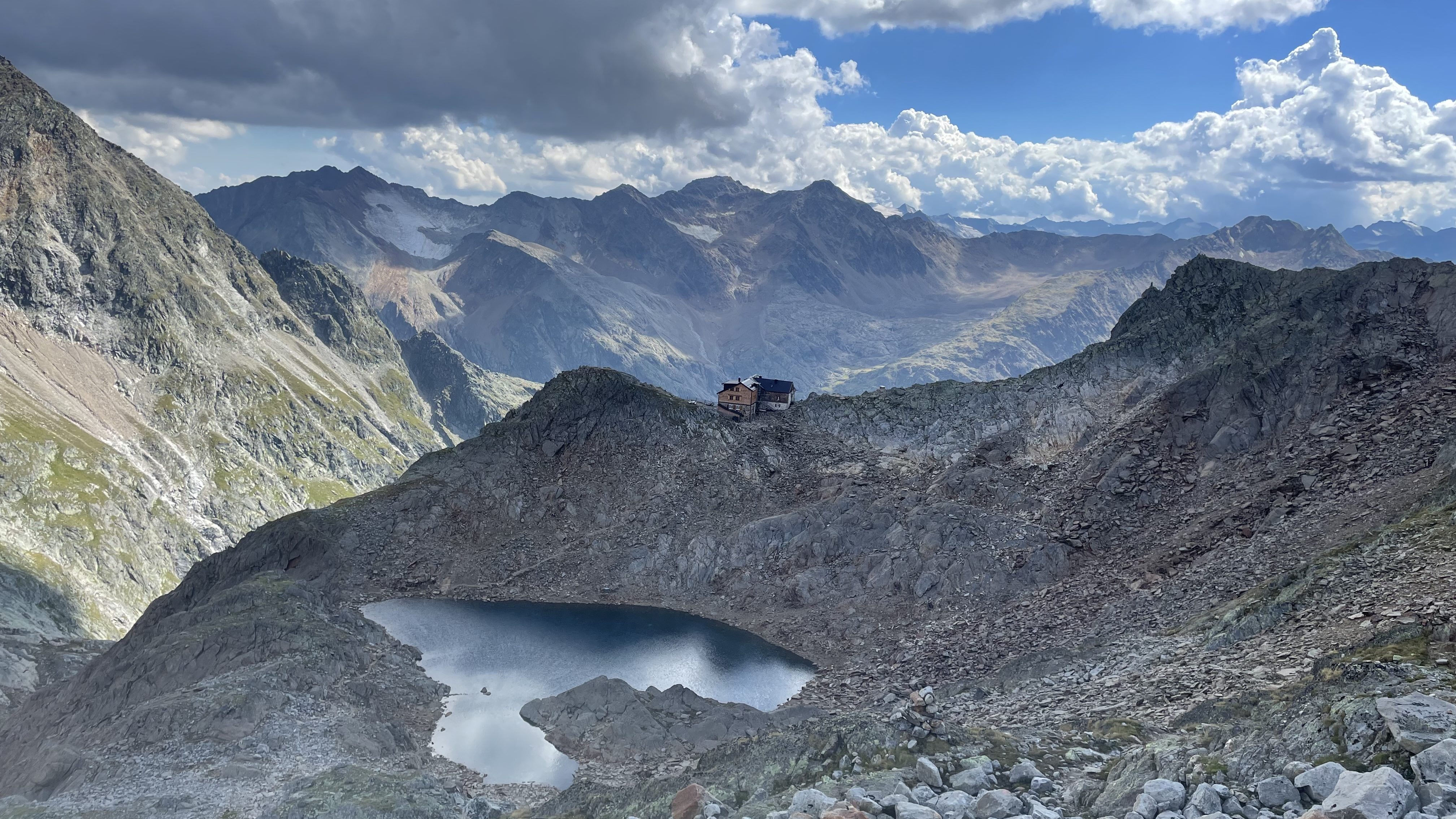 Hildesheimer Hütte von Norden fotografiert, der herzförmige See liegt unterhalb der Hütte, ein Weg führt dort hin, viele Felsen, im Hintergrund BErgkulisse