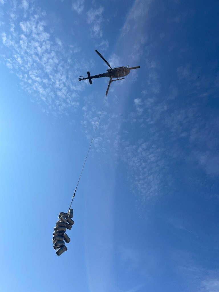 Hubschrauberversorgung der Hütte, Bierfässer hängen an einer langer Kette vom Helikopter herunter