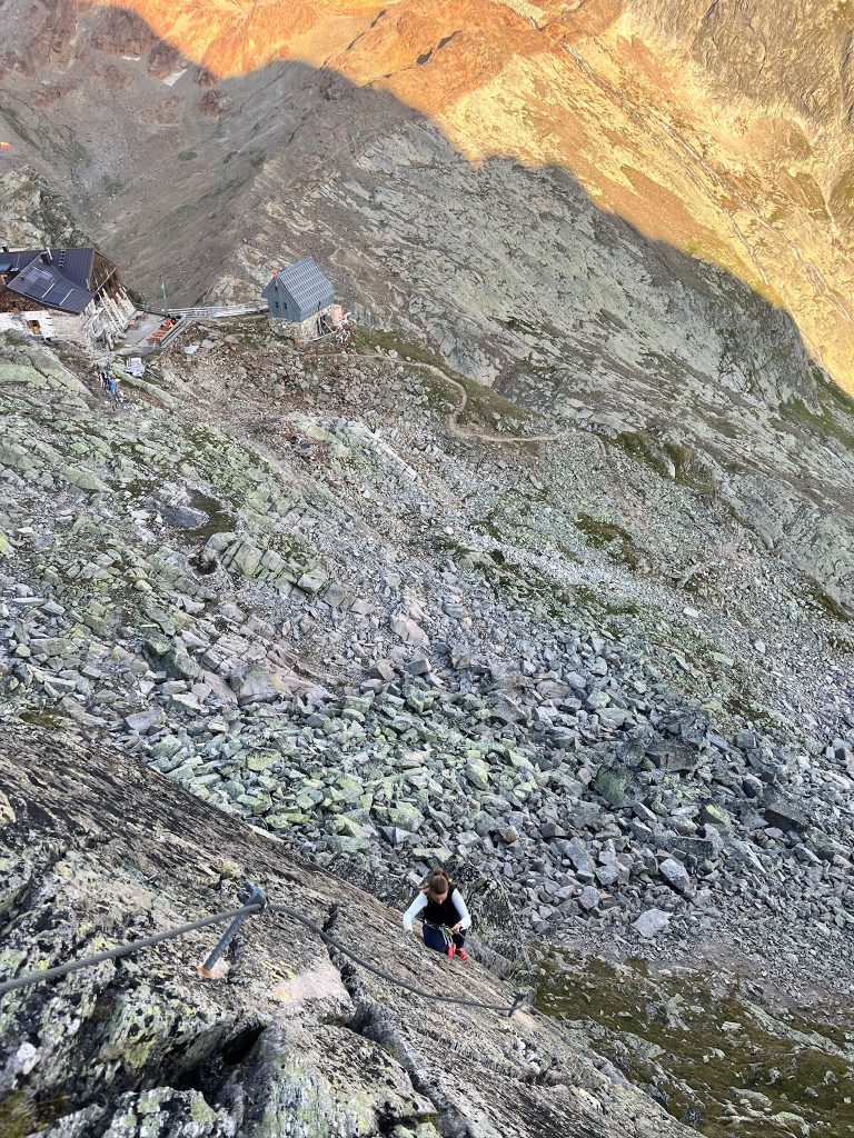 Person im Klettersteig, im Hintergrund die Hildesheimer Hütte recht nah beim Klettersteig