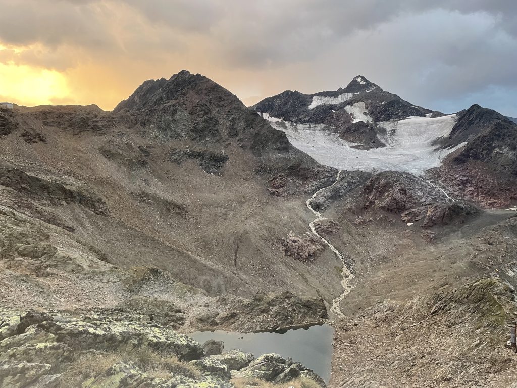 Blick auf die Pfaffenschneid Westflanke, der Gletscher ist schon aper, der Bach führt viel Wasser, rot-Gelbe Farben am Himmel