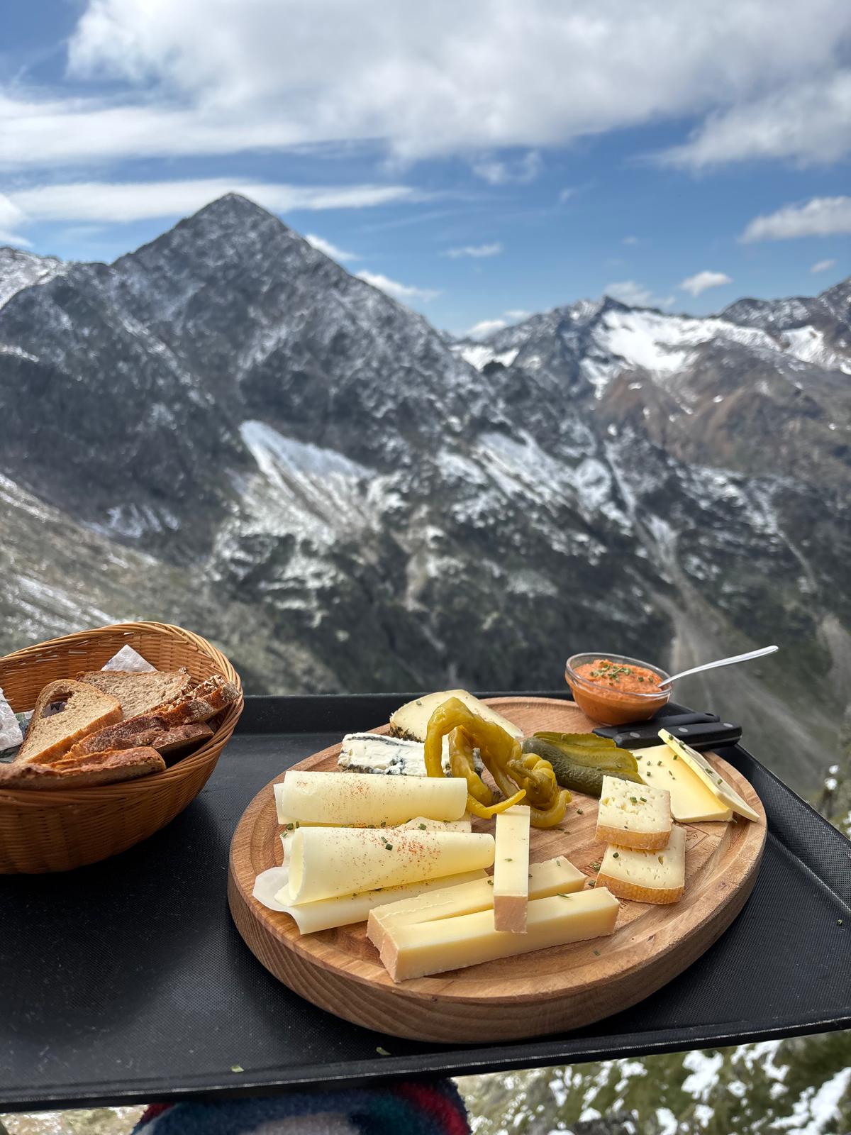vegetarische Brettljause mit Bergkäse, Bohnenaufstrich, Brotkorb, Chilikäse, Essiggurke, Pfefferoni, Blüten zur Dekoration, Gorgonzola... vor der Kulisse des Gaiskogels etwas unscharf im Hintergrund
