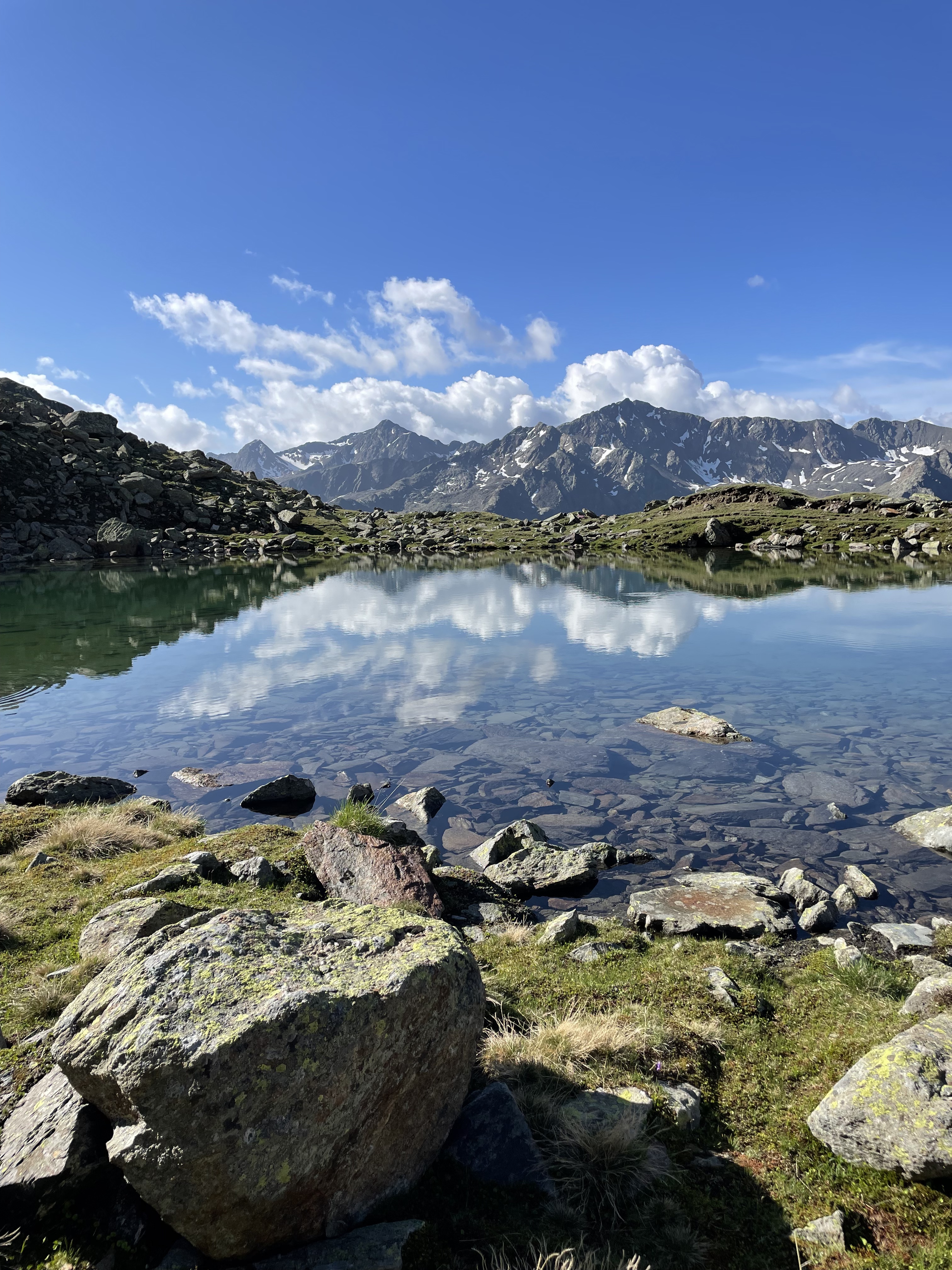 Blick über den Seekarsee, die Berge und Wolken spiegeln sich auf der glatten See-Oberfläche, das Bild strahlt Ruhe aus.
