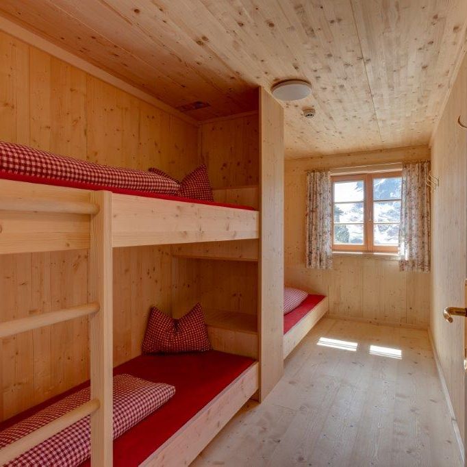 Zimmer von innen, rot karierte Bettwäsche in einem schönen, hellen Raum aus hellem Holz, die Sonne scheint beim Fenster herein